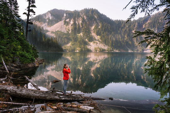 Female In Red Puffy Jacket Drinking Coffee Next To Alpine Lake