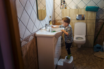 Small blonde boy standing on plstic steps and washing items in s