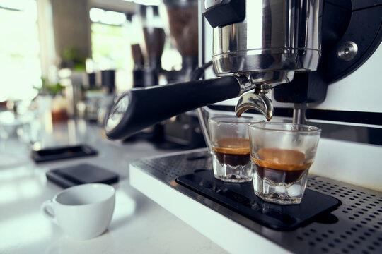 Two espresso shots being pulled into glasses from a machine.
