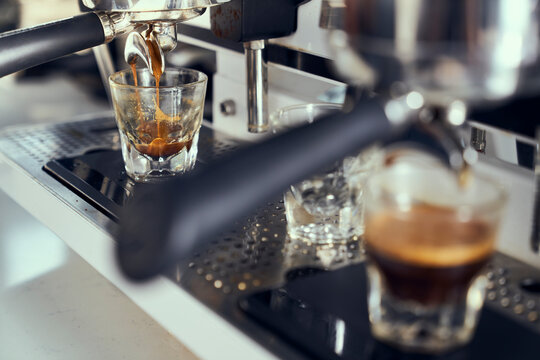 An espresso shot is pulled into a glass with out of focus foreground.
