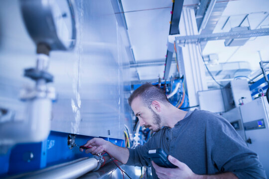 Young male engineer examining machine with multimeter in an industrial plant, Freiburg im Breisgau, Baden-W&uuml;rttemberg, Germany