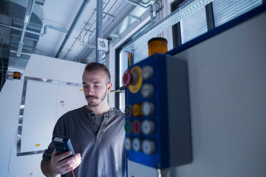 Young male engineer examining control panel with multimeter in an industrial plant, Freiburg im Breisgau, Baden-W&uuml;rttemberg, Germany