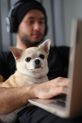 A stylish guy dressed in black clothes, with headphones, at home with his dog, work on a laptop, play board games, spend time together. The guy works on-line, makes purchases on a laptop, IT