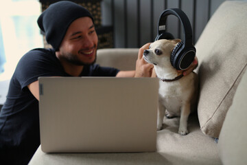 A stylish guy dressed in black clothes, with headphones, at home with his dog, work on a laptop, play board games, spend time together. The guy works on-line, makes purchases on a laptop, IT