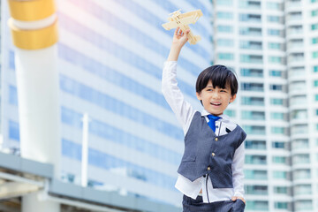 Happy asian boy playing with toy model of airplane in city Child pilot aviator with airplane dreams of traveling Little Asia boy get fun and enjoy his toy with smile face high building background