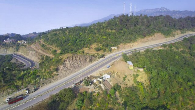 aerial drone shot flying towards wide 4 lane highway with cars, trucks and buses crossing and roads lower on the mountain visible, shot in himachal pradesh route to manali