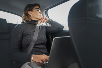 Fototapeta na wymiar Adult aattractive caucasian businesswoman using laptop while sitting on passenger seat of car