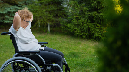 Elderly caucasian woman doing exercises while sitting in a wheelchair outdoors. 