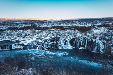 Iceland Hraunfossar orange sunrise over mountain landscape with frozen river waterfall in winter