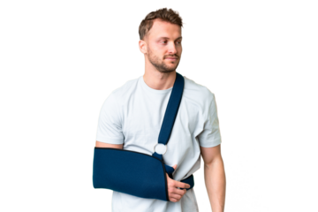Young caucasian man with broken arm and wearing a sling over isolated chroma key background looking to the side