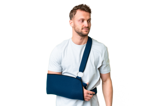 Young caucasian man with broken arm and wearing a sling over isolated chroma key background looking to the side