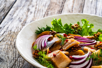 Marinated herrings with delicacies, walnuts and fresh vegetable leaves on wooden table
