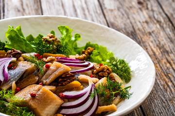 Marinated herrings with delicacies, walnuts and fresh vegetable leaves on wooden table
