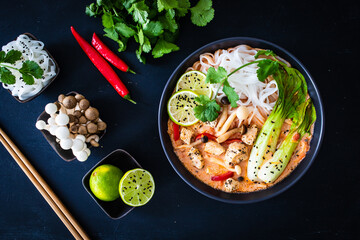 Tom Yum - Thai soup with chicken breast nuggets and noodles on wooden table
