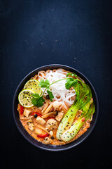 Tom Yum - Thai soup with chicken breast nuggets and noodles on wooden table
