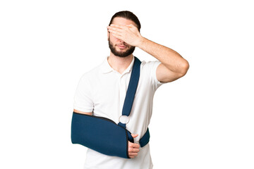 Young handsome man with broken arm and wearing a sling over isolated chroma key background covering...