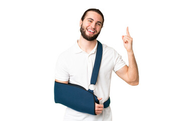 Young handsome man with broken arm and wearing a sling over isolated chroma key background showing...