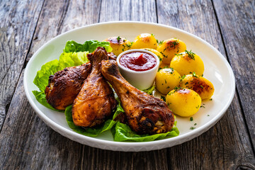Barbecue chicken drumsticks with fried potatoes, lettuce and ketchup on wooden table
