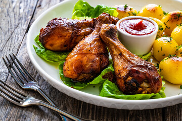 Barbecue chicken drumsticks with fried potatoes, lettuce and ketchup on wooden table
