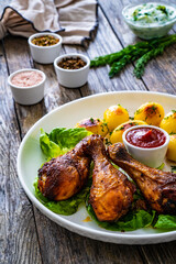 Barbecue chicken drumsticks with fried potatoes, lettuce and ketchup on wooden table
