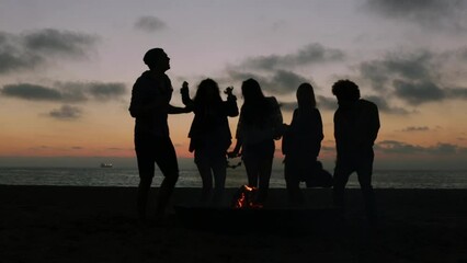 Silhouetted friends dancing around campfire at the beach