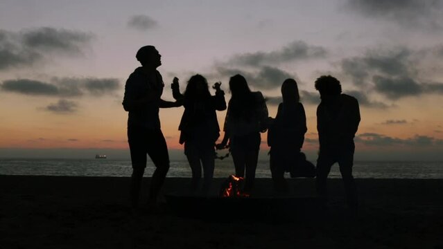 Silhouetted friends dancing around campfire at the beach
