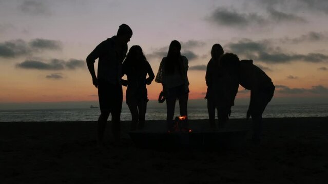 Silhouetted Friends Dancing Around Campfire At The Beach