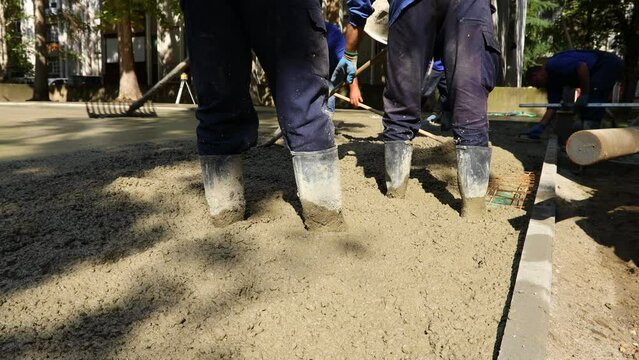 Construction workers, riggers are using rake to spreading, leveling concrete covering square reinforcement, pouring layer of concrete in foundation.