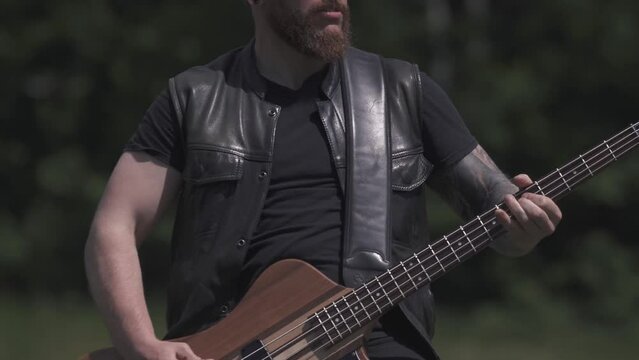 A man wearing leather plays rock metal on a bass guitar and sing outdo