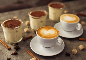 cups of cappuccino with three tiramisu cake with cinnamon sticks in the cosy cafe. High quality photo