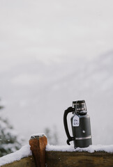 A growler filled with cold beer sits on snowy wooden railing outside