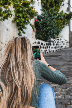 Woman with blonde hair doing a photo with her smartphone in the street