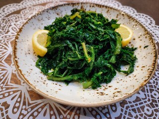 Boiled wild cooked greens close up top view, served with lemon and olive oil on a dish.