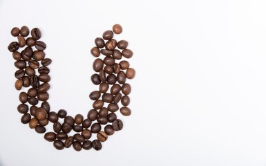 U is a capital letter of the English alphabet made up of natural roasted coffee beans that lie on a white background. Plenty of space to put text or pictures, top view and studio photography.