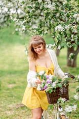 girl admires flowers in a spring garden. Portrait of a woman with a bicycle