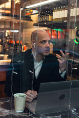 man young businessman entrepreneur caucasian,seriously enthusiast, bald in suit, sitting at a table, working laptop, talking via phone, remote job, in cafe window .concept entrepreneur lunch .
