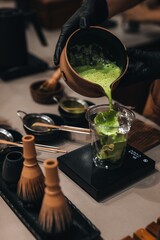 Matcha Japanese green tea making process. Female hands pouring matcha into a plastic cup....