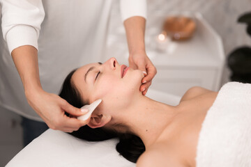 Obraz na płótnie Canvas Crop masseuse treating face of female client with kerokan tool