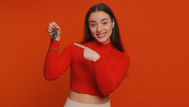 Pretty Young Woman In Crop Top Real Estate Agent Lifting Hand Showing The Keys Of New Home House Apartment, Buying, Renting Property, Mortgage Loan. Millennial Girl Isolated On Red Studio Background