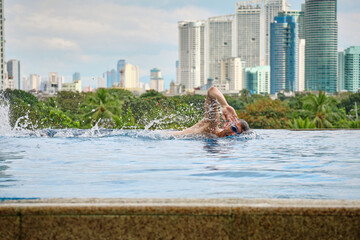 Manila, Philippines - Feb 02, 2020. A man swims a front crawl in a pool on the roof of a luxury hotel. View of the city of Manila from the pool of the luxury five-star Discovery Primea hotel.