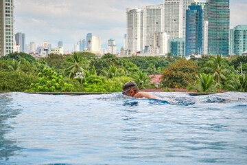 Manila, Philippines - Feb 02, 2020. A man swims a breaststroke in a pool on the roof of a luxury hotel. View of the city of Manila from the pool of the luxury five-star Discovery Primea hotel.