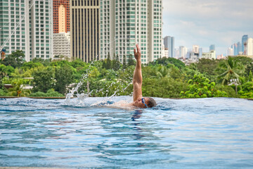 Manila, Philippines - Feb 02, 2020. A man swims a backstroke in a pool on the roof of a luxury hotel. View of the city of Manila from the pool of the luxury five-star Discovery Primea hotel.