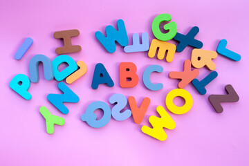 Colorful wooden alphabets on pink background.