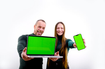 Use this new app. Cheerful couple point to smartphone and laptop with blank screen, recommend mobile app, advertise your website, mockup for design. chroma key green screen selective focus