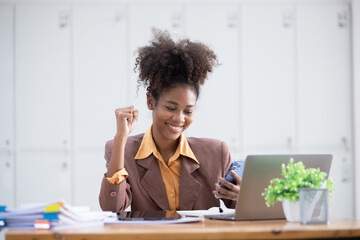 Young African American woman very happy and excited doing winner gesture with arms raised at table office, Business success and celebration concept.