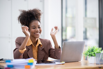 Young African American woman very happy and excited doing winner gesture with arms raised at table office, Business success and celebration concept.