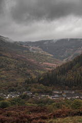 Fototapeta na wymiar A view from the top of the Rhondda Valley, in south Wales, on an autumn day, with low hanging clouds over the mountain top. A small community can be seen at the bottom of the mountain