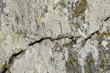 Big deep ascending crack on old moss-covered wall. Close-up. Copy space. Selective focus.