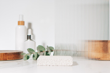 Spa and beauty product presentation scene made with porous stone podium near the cosmetic tubes and accessories on white bathroom shelf.