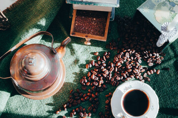 coffee grinder, coffee beans, a coffee pot and an old-fashioned coffee cup on a table with a green...